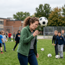 Soccer ball striking a coach's face during outdoor practice as students watch